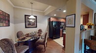 This single-floor residence offers a thoughtfully designed layout with a seamless flow between its main living areas. The kitchen is well-equipped with rich cherry wood cabinetry, granite-style countertops, tile flooring, and full black appliances including a side-by-side refrigerator, range, microwave, and dishwasher. Recessed lighting illuminates the space efficiently. Adjacent to the kitchen, the dining area features warm hardwood flooring, a tray ceiling with crown molding, and a pendant light overhead, creating an inviting atmosphere for meals. The living room continues the hardwood flooring and is finished with crown molding, a ceiling fan, and access to an exterior door that brings in natural light. Two bedrooms provide comfortable retreats, each carpeted and featuring ceiling fans. The primary bedroom includes an en-suite bathroom and exterior window views. Both bathrooms are finished with cherry wood vanities, granite-style countertops, tile flooring, and tub-shower combinations. Throughout the residence, neutral wall tones complement the warm wood tones of the cabinetry and flooring, creating a cohesive and welcoming interior aesthetic.