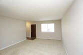 This thoughtfully laid-out space is spread across three floors, offering a versatile and functional layout suited to a variety of living arrangements. The interior design embraces a neutral, understated palette, with smooth white ceilings and light beige walls that create a bright, airy atmosphere throughout.

The living area is generously proportioned, featuring wall-to-wall neutral carpeting that adds warmth and comfort underfoot. The open layout allows for flexible furniture arrangements, making the space feel both expansive and welcoming. Clean white baseboards frame the room, contributing to the overall crisp and tidy appearance.

Natural light plays a key role in the ambiance of this space. A glass door or large window at the far end of the living area allows daylight to filter in, illuminating the interior and creating a seamless connection between the indoors and the outside. An elegant chandelier serves as a focal point in the adjoining area, adding a subtle touch of refinement to the otherwise minimalist design.

The transition between rooms is smooth and open, with the layout encouraging natural flow from one area to the next. The multi-floor configuration provides ample opportunity for defined living, sleeping, and utility zones, making this a highly practical and adaptable space.