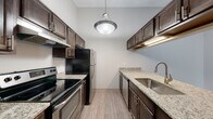 This single-floor residence offers a practical and well-organized layout across two bedrooms and two full bathrooms. The kitchen is efficiently designed with an L-shaped configuration, featuring white cabinetry trimmed in warm wood tones, light countertops, and white appliances including an electric range and refrigerator. A built-in range hood and ample upper and lower cabinet storage add to the kitchen's functionality. Tile flooring runs throughout the kitchen and bathrooms, providing easy maintenance in high-traffic areas.

A pass-through counter connects the kitchen to the main living area, which is finished with neutral carpet and features a ceiling fan with light fixture. The open layout allows for flexible furniture arrangement, with a hallway leading to the bedrooms and additional spaces. Both bedrooms are carpeted and offer closet access, with natural light provided by windows.

The two bathrooms are finished with tile flooring and include tub-shower combinations with white tile surrounds and vanities with storage. A dedicated laundry room houses a full-size washer and dryer alongside wire shelving for additional storage, adding considerable convenience to daily living.