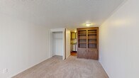 Located at 201 E Edgewood Blvd in Lansing, Michigan, this efficiently designed single-floor unit offers a practical and functional layout comprising a living area, a kitchenette, and a full bathroom. The main living space features neutral wall-to-wall carpeting and clean white walls, creating a bright and open feel. A prominent built-in wood bookcase with lower cabinet storage serves as a central architectural feature, adding warmth and character to the room. A textured ceiling runs throughout, complemented by crown molding that adds a subtle decorative touch. Natural light enters through a large window fitted with vertical blinds, while a wall-mounted HVAC unit provides in-unit climate control. A bifold-door walk-in closet offers convenient storage directly off the living area. The kitchenette, visible from the main room, includes wood-toned cabinetry, a countertop with sink, and a white range, all set on hardwood-style flooring. The bathroom features a wood-vanity with an integrated sink, a wall-mounted mirror cabinet, and direct access to the kitchenette area. This unit is well-suited for individuals seeking a straightforward, low-maintenance living space in a residential Lansing neighborhood.