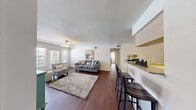 This thoughtfully designed 3-bedroom, 3-bathroom single-story home offers a comfortable and functional layout across its well-appointed rooms. The living area features rich dark hardwood-style flooring, a ceiling fan with light fixture, and large windows with French doors that fill the space with natural light and provide outdoor views. The open-concept design flows seamlessly into the dining area and kitchen, which is outfitted with light wood cabinetry, granite-style countertops, black appliances including a range, microwave, and refrigerator, and a convenient breakfast bar with bar seating. Each of the three bedrooms is carpeted for comfort and includes a ceiling fan, with windows dressed in sheer curtains and blinds that allow ample natural light. The primary bedroom features a bay-style window arrangement, creating an especially bright and airy retreat. All three bathrooms are finished with granite-style countertops, light wood vanity cabinetry, and large framed mirrors, with at least one bathroom offering a full tub-shower combination. Hardwood-style flooring extends through the bathrooms and hallway, tying the home together with a cohesive aesthetic. A connecting hallway provides practical circulation between the rooms, completing this well-organized and inviting home.
