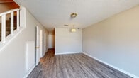 This two-story space is designed with a practical and straightforward layout, offering distinct living areas across both floors. The main level features open living and dining areas finished with durable wood-look plank flooring in a cool gray tone, complemented by neutral beige walls and textured ceilings. Pendant and flush-mount light fixtures provide overhead illumination throughout. A window on this level allows natural light to filter in, adding brightness to the space.

The kitchen is equipped with white cabinetry, warm wood-toned countertops, a double sink, and white appliances including a range and a full-size refrigerator. A window above the sink provides additional natural light. Also on the main level is a half bathroom featuring a vanity with a single sink and wood-look flooring.

A staircase connects to the upper level, where carpeted rooms offer a softer, quieter environment. These rooms each feature windows that bring in natural light and views of surrounding greenery. The upper level also includes a full bathroom outfitted with a combination tub and shower, a vanity, and wood-look flooring, providing all essential amenities in a clean, functional finish.