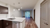 Located at 1800 S Jackson St in Seattle's vibrant Central District, this one-bedroom, one-bathroom unit offers a well-designed layout across a single floor. The open-concept living and kitchen area is anchored by rich hardwood-style flooring and flooded with natural light through expansive floor-to-ceiling sliding glass doors that open to an outdoor view of lush greenery. The kitchen is thoughtfully appointed with dark espresso cabinetry, white quartz countertops, a peninsula with an integrated sink, and a full suite of stainless steel appliances including a refrigerator, range, microwave, and dishwasher. Pendant lighting above the peninsula adds a modern, polished touch. The spacious bedroom features plush carpeting, a dedicated window with outdoor views, and generous closet storage. A second room with carpet provides flexible use as additional storage or a home office. The full bathroom includes a soaking tub and shower combo with tiled surround, a dark wood vanity with a white countertop, and a large mirror. Additional highlights include in-unit laundry, two closets, and a clean, contemporary aesthetic throughout with neutral tones and warm wood accents that create an inviting, comfortable atmosphere.