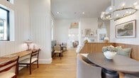 Located at 23615 Kingsland Blvd in Houston (Katy), TX, this single-floor space offers a thoughtfully designed interior that blends modern farmhouse aesthetics with refined comfort. The open layout is anchored by wide-plank light oak hardwood flooring that flows throughout, lending warmth and continuity to the entire area.

The central living room is the heart of the space, featuring soaring vaulted ceilings that amplify the sense of openness. A striking fireplace with a tiled surround and a clean white mantle serves as a focal point, framed by curated artwork and wall sconces. A built-in wood-paneled banquette provides fixed seating along one wall, accompanied by round pedestal tables and soft accent chairs — ideal for intimate gatherings or casual lounging.

Vertical shiplap wall paneling in crisp white adds architectural texture throughout, complementing the neutral palette of whites, warm taupes, and natural wood tones. Large black-framed windows invite abundant natural light, enhancing the airy ambiance. Hallways connect to adjacent rooms, one of which features a soothing blue accent wall, offering a subtle contrast to the otherwise bright, white interior.

Recessed lighting and a sculptural glass pendant fixture provide layered illumination, completing this polished, inviting communal space.