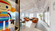 Located at 2140 N Miami Ave in Miami's vibrant Wynwood neighborhood, this single-floor space offers a generously proportioned open-plan layout that blends industrial and contemporary design with striking effect. Polished terrazzo flooring runs throughout the main area, reflecting abundant natural light that pours in through tall, floor-to-ceiling windows framing panoramic views of the Miami skyline and surrounding cityscape. The soaring ceiling features exposed white ductwork and structural elements, lending an industrial-chic character, while sleek pendant lighting and linear fixtures add a refined, modern touch. White paneled walls provide a clean, architectural backdrop that contrasts beautifully with the warm, textured interiors. A well-appointed bar area with a teal base, dark countertop, and barstool seating anchors one side of the space, illuminated by a bold geometric ring light fixture. A grand-scale lounge area dominates the open floor plan, defined by plush modular seating and low coffee tables. Sheer floor-to-ceiling drapery diffuses soft light in a quieter lounge zone, while large potted plants introduce organic warmth throughout. A wide entry corridor features large-format stone-look tile flooring and a dramatic dark feature wall, setting an impactful first impression. This space is ideal for premium events, showrooms, or creative professional use.
