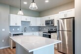 Located at 2692 Botanical Dr in Fitchburg, WI, this well-designed one-bedroom, one-bathroom unit offers a thoughtfully organized single-floor layout. The open-concept kitchen serves as the heart of the home, featuring crisp white shaker cabinetry, a light blue subway tile backsplash, quartz countertops, a spacious central island with pendant lighting, and a full suite of stainless steel appliances including a refrigerator, range, microwave, and dishwasher. Light hardwood flooring flows throughout, complementing the neutral, soft-toned walls. The living area extends naturally from the kitchen toward a private patio accessible through sliding glass doors dressed with vertical blinds, where a ceiling fan adds comfort and green outdoor views provide a serene backdrop. The bedroom is a well-proportioned retreat with a large window framing open landscape views, a ceiling fan, and built-in shelving for added storage. A dedicated closet offers organized storage with wire shelving and hanging space. The den provides flexible additional living space, while the in-unit laundry area houses a stacked Whirlpool washer and dryer. Recessed lighting throughout enhances the clean, modern aesthetic of this functional and inviting home.
