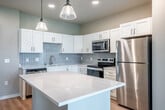 Located at 2692 Botanical Dr in Fitchburg, WI, this well-designed one-bedroom, one-bathroom unit offers a thoughtfully organized single-floor layout. The open-concept kitchen serves as the heart of the home, featuring crisp white shaker cabinetry, a light blue subway tile backsplash, quartz countertops, a spacious central island with pendant lighting, and a full suite of stainless steel appliances including a refrigerator, range, microwave, and dishwasher. Light hardwood flooring flows throughout, complementing the neutral, soft-toned walls. The living area extends naturally from the kitchen toward a private patio accessible through sliding glass doors dressed with vertical blinds, where a ceiling fan adds comfort and green outdoor views provide a serene backdrop. The bedroom is a well-proportioned retreat with a large window framing open landscape views, a ceiling fan, and built-in shelving for added storage. A dedicated closet offers organized storage with wire shelving and hanging space. The den provides flexible additional living space, while the in-unit laundry area houses a stacked Whirlpool washer and dryer. Recessed lighting throughout enhances the clean, modern aesthetic of this functional and inviting home.