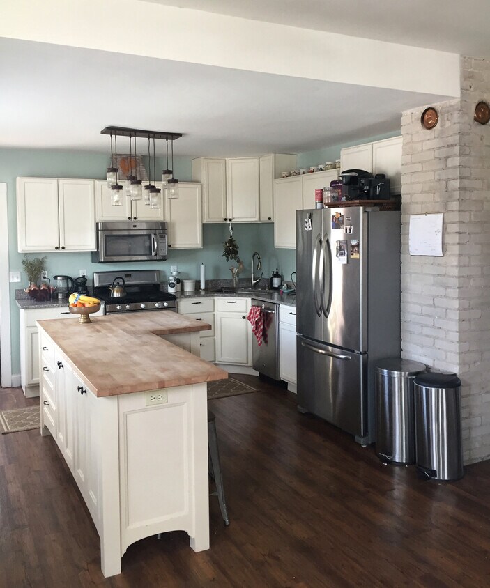 Spacious, open-concept kitchen with exposed brick, custom cabinets, granite countertops, island with butcher block countertop, and new stainless steel appliances. - 1201 29th Ave NE