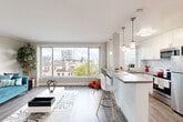 Located at 120 W Third Ave in San Mateo, CA, this well-appointed one-bedroom, one-bathroom residence offers a thoughtfully designed layout across a single floor. The open-concept living and kitchen area serves as the heart of the home, bathed in natural light from a large picture window that frames views of the surrounding San Mateo neighborhood and skyline. Wood-tone laminate flooring runs throughout, complementing the neutral, warm-toned walls.

The kitchen is a standout feature, outfitted with white shaker cabinetry, subway tile backsplash, grey quartz countertops, and stainless steel appliances including a dishwasher, range, and refrigerator. A peninsula with bar seating and elegant pendant lighting creates a natural division between the kitchen and living space while maintaining an open, airy feel.

The spacious bedroom offers a generous closet and a window with neighborhood views, providing a quiet, private retreat. The bathroom is clean and modern, finished in white with a tub/shower combination and a wall-mounted shelving unit.

A hallway connects the main living areas to the bedroom and bathroom, adding to the functional flow of the layout. Throughout the residence, the design emphasizes clean lines, bright finishes, and practical use of space.