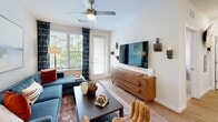 Located at 1300 Hendricks Ave in Jacksonville, Florida, this one-bedroom, one-bathroom residence offers a thoughtfully designed open-concept layout across a single floor. The combined kitchen and living area serves as the heart of the home, where light hardwood flooring flows throughout. The kitchen is outfitted with crisp white shaker cabinetry, granite countertops, a tile backsplash, stainless steel appliances, and a center island with seating — ideal for casual dining or entertaining. Pendant lighting above the island adds a polished touch. The living room is bright and inviting, with large windows that welcome natural light and a ceiling fan overhead. A door provides direct outdoor access, enhancing the open feel of the space. The bedroom is a comfortable retreat featuring plush carpeting, a ceiling fan, a window with outdoor views, and a dedicated walk-in closet with built-in wire shelving for organized storage. The bathroom includes a spacious walk-in glass-door shower with tile surround and built-in open shelving for linens — a clean, functional design. Throughout the residence, neutral tones and modern finishes create a cohesive, contemporary ambiance.