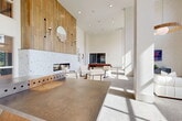 Located at 2700 N Lake Forest Dr in McKinney, TX, The Sylvan at Painted Tree offers a thoughtfully designed single-floor community clubhouse that blends contemporary architecture with warm, natural materials. The spacious open-plan layout is anchored by soaring double-height ceilings that amplify the sense of volume throughout. A dramatic floor-to-ceiling wood-paneled accent wall frames a sleek mosaic-tiled fireplace, creating a striking focal point in the main lounge area. A sculptural concrete-topped table with a wood pedestal base serves as both a functional and artistic centerpiece. The lounge area features plush white seating and a striking live-edge wood coffee table, positioned in front of large black-framed floor-to-ceiling windows that flood the space with natural light and offer views of the surrounding outdoor landscape. A billiards table and curated wall art add a recreational dimension to the space. The dining area showcases arched architectural details, large-format light tile flooring, and natural rattan seating arranged around communal tables, all beneath soaring ceilings with abundant recessed lighting. Throughout the space, a neutral palette of whites and warm wood tones creates a cohesive, inviting ambiance that is both modern and welcoming.