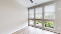 Located at 651 Meeting St in the heart of Charleston, SC, this single-floor residence offers a clean, contemporary aesthetic with a bright and airy ambiance throughout. Light hardwood-style flooring flows consistently across the living spaces, creating a sense of warmth and cohesion.

The spacious living area is a standout feature, boasting expansive floor-to-ceiling windows fitted with horizontal blinds that flood the room with natural light and frame lush tree-top views of the surrounding neighborhood. Ceiling fans add both comfort and style to the open layout.

The kitchen is efficiently designed with white cabinetry, light countertops, and a classic white subway tile backsplash. Stainless steel appliances, including a range, over-the-range microwave, and dishwasher, provide a polished, modern finish.

The bedroom is well-proportioned and includes a reach-in closet with built-in shelving, served by a ceiling fan and neutral wall tones that promote a restful atmosphere.

The bathroom is thoughtfully appointed with a full tub-shower combination featuring white tile surround, wood-look vinyl flooring, and a tall gray storage cabinet that adds practical storage. Crisp white walls and fixtures maintain the home's clean, modern character throughout. This residence offers a comfortable and stylish living experience in one of Charleston's vibrant neighborhoods.
