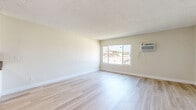 Located at 18540 Plummer Street in the Northridge neighborhood of Los Angeles, this single-floor unit offers a well-organized layout comprising a living room, kitchen, and full bathroom. Light wood-style flooring runs throughout the space, contributing to a clean, modern aesthetic that is complemented by neutral beige walls and white trim.

The living room is the largest area of the unit, bathed in natural light from a wide, multi-pane window that offers views of the surrounding neighborhood, including glimpses of palm trees. A wall-mounted air conditioning unit provides climate control, and a textured popcorn ceiling adds a classic residential character. An adjacent closet with built-in shelving and hanging rods offers practical storage.

The galley-style kitchen is efficiently designed with white cabinetry lining both sides, dark granite-look countertops, a stainless steel sink, and a white electric range with overhead ventilation. The layout maximizes every inch of available space and maintains the same light flooring found throughout the unit.

The bathroom features a tub and shower combination enclosed by sliding frosted glass doors with chrome framing, paired with white tile surround and a standard toilet. The overall design of the space is straightforward, clean, and functional, making it a practical option in the Los Angeles area.