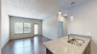 This contemporary single-floor residence in Independence, Missouri offers a thoughtfully designed open-concept layout that seamlessly connects the kitchen and living areas. The kitchen is a standout feature, showcasing dark espresso cabinetry, stainless steel appliances including a refrigerator, range, and microwave, light quartz countertops, a tiled backsplash, and a central island with pendant lighting. Wood-style flooring flows throughout the main living areas, adding warmth and continuity to the space.

The living area is bright and airy, benefiting from natural light through large windows with blinds and direct access to an outdoor balcony. The bedrooms are carpeted for comfort, with one featuring multiple windows, a ceiling fan, and ample natural light, while another includes a built-in closet with a hanging rod. The bathrooms are well-appointed; one features a wide quartz vanity countertop, dark cabinetry with modern hardware, a large mirror, and a glass-enclosed shower, while the second includes a full soaking tub with shower, a single vanity, and wood-look flooring. The overall aesthetic is clean, modern, and functional throughout.