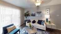 This single-floor residence offers a thoughtfully designed layout that maximizes both comfort and functionality. The living room serves as the heart of the home, featuring warm hardwood-style flooring, a ceiling fan with light fixture, and a large sliding glass door framed by vertical blinds that floods the space with natural light and provides access to the outdoors. The open layout connects seamlessly to the dining area, which is anchored by a round table beneath a pendant light fixture and accented by a window with blinds, creating a bright and inviting space for meals and gatherings. The galley-style kitchen is equipped with dark espresso cabinetry, granite-style countertops, black appliances including a refrigerator and range, and a double stainless steel sink — offering ample storage and prep space in an efficient corridor layout. The bedroom is a calm retreat featuring plush carpeting, a ceiling fan, a window for natural light, and direct access to the en-suite bathroom. The bathroom includes dark cabinetry, granite-style countertops, a full tub-shower combination, and wood-style flooring. Throughout the residence, textured ceilings, neutral wall tones, and consistent design choices create a cohesive and modern aesthetic.