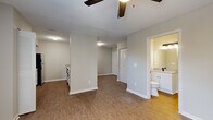 This single-floor unit offers a clean, modern aesthetic throughout, highlighted by warm wood-look flooring and a neutral color palette that creates a bright and cohesive atmosphere. The open-concept living area is anchored by a ceiling fan and receives natural light through a large window, offering pleasant outdoor views. A pass-through peninsula counter connects the living space to the kitchen, creating an easy flow between the two areas. The kitchen is well-equipped with stainless steel appliances — including a refrigerator, electric range, microwave, and dishwasher — complemented by crisp white cabinetry with matte black hardware and a double-basin sink. A washer unit is also conveniently tucked within the kitchen area. The bedroom is generously sized, featuring a ceiling fan with light fixture, a louvered bi-fold closet, and a window that brings in natural light. The bathroom is finished with a white shaker-style vanity, a light stone-look countertop, a large mirror with a modern three-bulb vanity light, and matte black fixtures that add a contemporary touch. An electrical panel is accessible near the entry area. Throughout the unit, clean white trim and consistent flooring tie all spaces together for a polished, move-in-ready feel.
