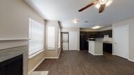 This single-story residence offers a well-organized layout with a cohesive design palette carried throughout. The open living area is finished with rich, dark wood-style flooring and features a ceiling fan overhead, while large windows fitted with white horizontal blinds allow ample natural light to fill the space. A textured ceiling adds architectural character throughout the home.

The kitchen is positioned adjacent to the living area and features dark espresso cabinetry, black appliances including a refrigerator, range, and built-in microwave, along with a peninsula counter finished in light granite-style laminate that provides additional workspace and a casual dining option. A dedicated in-unit laundry alcove with a stacked washer and dryer is conveniently located nearby.

The bedrooms are carpeted and each includes a ceiling fan with light fixture and windows providing natural light. One bedroom offers direct access to a private en-suite bathroom, which features a double vanity with dark cabinetry, granite-style countertops, a soaking tub, and a separate shower enclosure. A second bathroom mirrors the same design, with a dark-framed vanity mirror and granite countertop. The overall aesthetic is consistent and functional throughout.