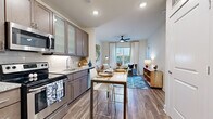 Located at 2142 Commonwealth Ave in Charlotte's vibrant 28205 corridor, this single-floor residence offers a thoughtfully designed open-concept layout that seamlessly connects the kitchen, dining, and living areas. The kitchen is well-equipped with stainless steel appliances — including a refrigerator, range, and over-the-range microwave — complemented by warm taupe cabinetry with frosted glass accents, granite countertops, and a classic subway tile backsplash. A high-top dining table positioned adjacent to the kitchen provides a casual yet functional dining space. Hardwood-style flooring runs throughout the main living areas, lending warmth and continuity to the space. The living room is bright and inviting, featuring a ceiling fan, large windows dressed with floor-length curtains, and views of the surrounding neighborhood. The bedroom is generously sized with ample natural light from wide windows and a ceiling fan overhead. The bathroom is finished with large-format tile flooring, a granite vanity, and a full soaking tub with tiled surround. Throughout the residence, neutral tones, recessed lighting, and clean architectural lines create a polished, contemporary ambiance suited for comfortable everyday living.