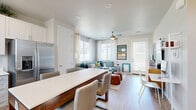 Located in San Tan Valley, AZ, this single-story, one-bedroom, one-bathroom residence offers a thoughtfully designed layout with modern finishes and a bright, cohesive aesthetic throughout. Light-toned wood-look flooring runs continuously across all rooms, tying the space together seamlessly.

The living room is a welcoming area featuring dual windows dressed with sheer white curtains that invite abundant natural light. A ceiling fan adds comfort, and a private exterior door provides convenient outdoor access.

The kitchen is a standout feature, outfitted with crisp white shaker cabinetry extending to the ceiling, quartz countertops, and a full suite of stainless steel appliances including a refrigerator with ice maker, range, microwave, and dishwasher. A large kitchen island with a wood base and quartz top offers additional seating and workspace, complemented by recessed lighting overhead.

The bedroom is a serene retreat highlighted by an elegant arched accent wall, a ceiling fan, and a well-sized window with views to the outside. A dedicated closet and convenient hallway access complete the room's practical layout.

The bathroom is finished with a white vanity, quartz countertop, a large mirror, and a sliding glass-door shower, all bathed in natural light from a window above.