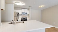 Located at 1405 Riverview Pl in Jonesboro, Georgia, this single-story residence offers a thoughtfully designed layout with a clean, contemporary aesthetic. The open-concept kitchen serves as a central highlight, featuring crisp white cabinetry, bright white countertops, and a suite of stainless steel appliances including a refrigerator, range, microwave, and dishwasher. A wide peninsula with an undermount sink and a flexible faucet extends into the living area, creating a natural flow between cooking and entertaining spaces. Light wood-style flooring runs throughout the main living areas, complementing the neutral warm-beige wall tones and white trim for a cohesive, inviting atmosphere. The living area benefits from multiple windows dressed with horizontal blinds, allowing ample natural light while providing outdoor views of the surrounding greenery. Ceiling fans are featured in the main living spaces and bedrooms, enhancing comfort year-round. The bathroom is well-appointed with white cabinetry, a framed mirror, light countertops, and a tub-shower combination. A dedicated laundry area with an in-unit washer and dryer adds everyday convenience. The overall ambiance is bright, clean, and functional.