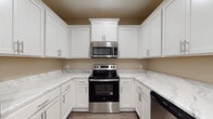 Located at 4750 Mac Rd in Valdosta, Georgia, this single-floor residence offers a clean, modern aesthetic with consistent design choices throughout. The kitchen is a standout feature, showcasing crisp white shaker-style cabinetry with brushed nickel hardware, striking marble-look countertops, and a full suite of stainless steel appliances including an electric range, over-the-range microwave, and dishwasher. The U-shaped layout maximizes counter and storage space, making it both functional and visually appealing. The living areas are finished with rich, dark hardwood-style flooring that runs seamlessly throughout the home, complemented by warm neutral-toned walls and clean white trim and baseboards. Ceiling fans with light fixtures are present in the main living and bedroom spaces, promoting comfort and air circulation. The bedroom offers a bright, airy feel, enhanced by a window dressed with white horizontal blinds that allow natural light to filter in. Multiple interior doors with panel detailing add architectural character to the layout. The bathroom is outfitted with a white vanity, a combination tub and shower unit, and matching hardwood-style flooring, maintaining the cohesive design language of the home. Overall, the space presents a fresh, move-in-ready interior with practical, modern finishes.