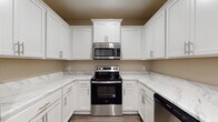 Located at 4750 Mac Rd in Valdosta, Georgia, this single-floor residence offers a clean, modern aesthetic with consistent design choices throughout. The kitchen is a standout feature, showcasing crisp white shaker-style cabinetry with brushed nickel hardware, striking marble-look countertops, and a full suite of stainless steel appliances including an electric range, over-the-range microwave, and dishwasher. The U-shaped layout maximizes counter and storage space, making it both functional and visually appealing. The living areas are finished with rich, dark hardwood-style flooring that runs seamlessly throughout the home, complemented by warm neutral-toned walls and clean white trim and baseboards. Ceiling fans with light fixtures are present in the main living and bedroom spaces, promoting comfort and air circulation. The bedroom offers a bright, airy feel, enhanced by a window dressed with white horizontal blinds that allow natural light to filter in. Multiple interior doors with panel detailing add architectural character to the layout. The bathroom is outfitted with a white vanity, a combination tub and shower unit, and matching hardwood-style flooring, maintaining the cohesive design language of the home. Overall, the space presents a fresh, move-in-ready interior with practical, modern finishes.