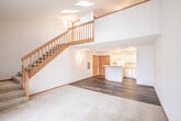 Located at 1070 N Pleasant View Rd in Madison, WI, this two-story home offers a well-organized layout spread across two floors. The main level features an open-concept kitchen and living area with durable hardwood-style flooring throughout. The kitchen is equipped with white cabinetry, white appliances including a range and dishwasher, and a central peninsula that provides additional counter space and separates the kitchen from the living area. The living room benefits from natural light through a sliding glass door and features a mix of hardwood-style flooring and carpet, with a wood-railed staircase leading to the upper level. Vaulted ceilings in the living area create an airy, open feel. Upstairs, the generously sized bedroom is carpeted and features vaulted ceilings, a ceiling fan, and a large closet with bifold doors, offering ample storage. The full bathroom on the upper level includes a wide vanity with a large mirror, modern fixtures, and hardwood-style flooring, conveniently positioned near the bedroom. Warm wood trim accents are found throughout the home, lending a cohesive and inviting character to each space.