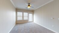 Located at 2515 W San Antonio St in New Braunfels, TX, this single-story unit offers a well-designed layout with a blend of hardwood-style and plush carpeted flooring throughout. The entryway opens into a living area with warm, neutral tones and recessed lighting, transitioning seamlessly into the galley-style kitchen. The kitchen is outfitted with dark espresso cabinetry extending to the ceiling for maximum storage, light granite countertops, a stainless steel sink, and black appliances including a full-size refrigerator. The bedrooms feature plush carpet, crown molding, ceiling fans, and window blinds that allow for natural light control. One bedroom includes a private exterior door. A dedicated in-unit laundry room houses a full-size washer and dryer with additional shelving above. The bathrooms are finished with dark vanity cabinetry, granite countertops, wood-look tile flooring, and a full tub-shower combination with white tile surround. A second bathroom offers an expansive vanity with a large mirror and ample cabinet storage. The unit's consistent use of neutral warm beige tones and quality finishes throughout creates a cohesive and comfortable living environment.