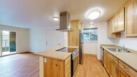 This single-floor, 3-bedroom, 1-bathroom home offers a practical and comfortable layout designed for everyday living. The open-concept kitchen and living room serve as the heart of the home, featuring warm natural wood cabinetry, neutral countertops, and a central island with a built-in cooktop topped by a stainless steel range hood. Stainless steel appliances, including a refrigerator and range, complement the kitchen's clean aesthetic, while light hardwood flooring runs throughout the main living areas, adding warmth and continuity. A ceiling fan in the living area provides comfort, and a sliding glass door opens to an outdoor area, filling the space with natural light and providing easy access to the exterior. The three bedrooms offer a quiet retreat, with plush carpet flooring, built-in closets, and windows that let in natural light. The primary bedroom is generously sized, providing comfortable living space. The shared bathroom is efficiently designed, featuring a wooden vanity with drawers, a countertop sink, and a well-placed mirror with overhead lighting. A connecting hallway ties all rooms together, ensuring a cohesive flow throughout the home. Wall heaters are present in several rooms, providing efficient climate control throughout.