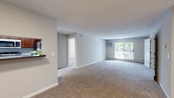 Located in Eden Prairie, Minnesota, this well-designed one-bedroom, two-bathroom residence offers a comfortable and functional layout across a single floor. The open-plan kitchen and living area forms the heart of the home, with the kitchen featuring warm wood cabinetry, stainless steel appliances including a refrigerator, range, and microwave, and light wood-look flooring that adds a clean, modern touch. The spacious living room is carpeted and bathed in natural light, with a sliding glass door leading to an outdoor balcony area overlooking lush greenery and a pool beyond. A wall-mounted air conditioning unit and baseboard heating ensure year-round comfort. The generously sized primary bedroom is also carpeted, fitted with a ceiling fan and light fixture, and enjoys its own window with outdoor views. Both bathrooms are well-equipped, featuring tub-shower combinations and hexagonal tile flooring; the primary bathroom includes a rich wood vanity with a light stone countertop and a large mirror. A dedicated laundry area houses a top-loading washer with overhead shelving for added storage. A closet completes the layout, offering practical organization. Textured ceilings are found throughout, lending a classic residential character to the space.