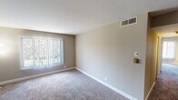 Located at Jefferson Square in Elk Grove Village, IL, this single-floor residence offers a practical and comfortable layout. The living area is generously sized, featuring plush carpeting, neutral taupe walls, and a ceiling fan overhead. A large window fitted with vertical blinds allows natural light to filter in while providing views of the surrounding greenery. An open pass-through connects the living space directly to the kitchen, enhancing the sense of openness.

The kitchen is well-appointed with light wood cabinetry, mosaic tile backsplash in earthy tones, stainless steel appliances including a range, over-the-range microwave, and dishwasher, complemented by light countertops and hardwood-style flooring. Ample upper and lower cabinet storage provides excellent functionality.

The bedrooms are carpeted and finished with the same neutral palette, each offering closet access and natural light through windows with outdoor views. Two bathrooms serve the unit: one features a white vanity with a large mirror and warm vanity lighting, while the other includes a shower-tub combination with a full-length curtain, a single-basin vanity, and a wall-mounted mirror. Throughout, clean white trim and consistent finishes contribute to a cohesive, well-maintained ambiance.