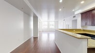 Located in the heart of Downtown Los Angeles at 215 W 5th Street, this 2-bedroom, 1-bathroom residence offers a well-designed single-floor layout with a clean, modern aesthetic. Rich hardwood flooring flows throughout the main living areas and bedrooms, providing warmth against the crisp white walls and recessed lighting overhead.

The open-concept kitchen and living area form the centerpiece of the home. The kitchen is outfitted with deep espresso-toned cabinetry, granite countertops, stainless steel appliances including a refrigerator and microwave, and a peninsula that provides additional prep space and naturally separates the kitchen from the living area. Stone tile flooring grounds the kitchen zone, transitioning seamlessly to the hardwood of the living space.

The spacious living room benefits from large windows that frame views of the surrounding Downtown LA architecture, allowing abundant natural light to fill the interior. The primary bedroom is a well-proportioned retreat with hardwood floors and direct access to the full bathroom, which features dark wood vanity cabinetry and granite countertops consistent with the kitchen's design language. The second bedroom offers similar clean finishes with its own large windows overlooking the urban streetscape. A utility area with stone tile flooring completes the layout.