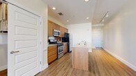This single-floor residence features a thoughtfully organized layout encompassing three bedrooms, two bathrooms, a kitchen, living room, dedicated laundry area, and a walk-in closet. Warm-toned hardwood-style flooring flows consistently throughout the main living areas, creating a cohesive and inviting atmosphere.

The kitchen serves as a central hub, featuring warm wood cabinetry, a tile backsplash, stainless steel appliances including a gas range, microwave, and refrigerator, and a freestanding island with a granite-style countertop and integrated sink. The open sightline from the kitchen extends down a hallway toward the bedrooms, enhancing the sense of space.

The primary bedroom is a comfortable size, featuring a notable architectural column, rich hardwood-style flooring, and direct access to a bathroom. A separate bedroom benefits from a large bank of triple windows offering urban views and abundant natural light. The primary bathroom includes both a soaking tub with tile surround and a separate glass-enclosed shower stall with tile flooring.

A walk-in closet provides wire shelving on multiple walls for organized storage, while the laundry area houses a stacked washer and dryer unit for added convenience.
