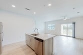Located at 21101 Panama City Beach Pkwy in Panama City Beach, Florida, this modern single-floor unit offers a bright, contemporary layout designed for comfortable coastal living. The open-concept main living area is anchored by a well-appointed kitchen featuring light wood cabinetry, a granite-topped island with an undermount sink, stainless steel appliances including a range, microwave, and refrigerator, and a subway tile backsplash. The island flows seamlessly into a generous living space finished with light wood-style flooring and recessed lighting throughout. Ceiling fans are present in the living area and bedrooms, contributing to a comfortable and airy atmosphere. Sliding glass doors and large windows allow natural light to fill the space and provide outdoor views. The bedrooms are well-sized, each with ample natural light courtesy of windows with blinds. The primary bathroom includes a dual-sink vanity with granite countertops, illuminated mirrors, and a soaking tub with shower. A secondary bathroom offers a walk-in shower with a clean, all-white tile finish. A dedicated laundry room houses a full-size washer and dryer with overhead wire shelving, adding practical convenience to the unit's overall functional design.