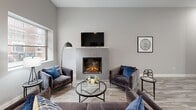 Located at 1000 Elm St in Manchester, NH, this well-appointed unit offers a thoughtfully designed single-floor layout with a cohesive contemporary aesthetic throughout. The living room serves as the focal point of the space, anchored by a striking herringbone-tiled fireplace with a mounted television above, wood-look flooring, and ample natural light from street-facing windows that frame views of the surrounding neighborhood. Adjacent to the living area, a dedicated dining space features clean lines and tall ceilings that lend an open, airy feel to the room. The kitchen is a standout feature, boasting tall white shaker cabinetry extending to the ceiling, stainless steel appliances including a French door refrigerator and electric range, quartz countertops, a generous peninsula with pendant lighting overhead, and bold blue bar seating. The bedroom is carpeted for comfort and includes a walk-in closet and direct access to additional storage. The bathroom presents a clean, modern finish with a double-sink vanity, wood-look tile flooring, and a full tub-shower combination. Throughout the unit, a neutral gray palette, consistent flooring, and modern fixtures create a polished, move-in-ready environment.