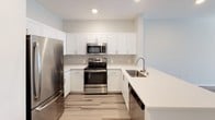 Located at 8707-8747 Fletcher Pkwy in La Mesa, California, this single-floor residence offers a clean, modern design with an open and functional layout. The living area features light-toned wood-style flooring and a ceiling fan with integrated lighting, creating a bright and airy atmosphere. Natural light filters in through window blinds, enhancing the sense of openness throughout the space.

The kitchen is a standout feature, showcasing white shaker-style cabinetry, a neutral tile backsplash, and quartz countertops. Stainless steel appliances — including a refrigerator, range, and over-the-range microwave — provide a modern, cohesive aesthetic. The kitchen opens toward the living area via a peninsula counter, promoting a seamless flow between spaces.

The bedroom continues the light and neutral palette, with soft carpeting underfoot, a ceiling fan, and a window dressed with horizontal blinds for privacy and light control.

The bathroom is finished with wood-style vinyl flooring, a white vanity with an integrated sink, a large mirror, and a full tub-and-shower combination. Clean white walls and modern fixtures give the bathroom a fresh, contemporary feel.

Overall, this residence presents a well-maintained, move-in-ready space with consistent modern finishes throughout, ideal for comfortable everyday living in La Mesa.