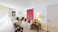 Located at 2045 Sibley Rd in Augusta, Georgia, this single-floor home offers a thoughtfully arranged layout designed for comfortable everyday living. The living room serves as a warm and inviting centerpiece, featuring neutral carpet flooring, a textured ceiling, and a large window dressed with sheer red curtains that allow natural light to fill the space. The kitchen is efficiently designed with light wood cabinetry, a breakfast bar counter, and full appliances including a refrigerator and microwave, with direct adjacency to a dining area that comfortably accommodates a full dining set. The bedroom is a restful retreat, complete with a ceiling fan, natural light from a window with sheer draping, and ample space for a queen bed and dresser storage. The bathrooms are clean and functional — one features a full tub-shower combination with white tile surround, while another includes a well-lit vanity with a large mirror and warm overhead lighting. Throughout the home, the interiors maintain a consistent palette of light, neutral tones, contributing to a cohesive and calm atmosphere. The layout flows naturally between spaces, making this home a practical and comfortable residence in Augusta.