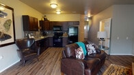 This two-story residence is thoughtfully laid out across two levels, blending functionality with comfortable living. The main level centers around an open-concept living and kitchen area, where wood-look flooring runs throughout. The kitchen is equipped with dark espresso cabinetry extending to the ceiling for ample storage, black appliances including a refrigerator, range, built-in microwave, and a sink set into light-toned countertops with a tile backsplash. The adjoining living area is generously sized and features a sliding glass door that invites natural light and provides access to an outdoor space. A half bathroom and a dedicated laundry room with a full-size washer and dryer and overhead shelving are also located on the main level. A carpeted staircase with a white handrail leads to the upper floor, where the bedrooms are situated. Each bedroom features carpet flooring and windows with blinds. At least one bedroom includes a walk-in closet with built-in shelving. A full bathroom on the upper level offers a tub-shower combination with chrome fixtures and wood-look tile flooring. Neutral wall tones and consistent finishes throughout create a cohesive and practical living environment.