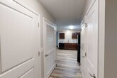 This single-floor, three-bedroom, two-bathroom residence at 100 Codell Drive in Lexington, Kentucky offers a practical and well-appointed layout. Light wood-look luxury vinyl flooring runs throughout the entire unit, creating a cohesive and easy-to-maintain living environment. A central hallway connects the main living areas, lined with clean white doors—including a louvered closet door—leading to various rooms. The kitchen is a standout feature, showcasing rich dark walnut cabinetry, light granite-style countertops, a tile backsplash, and a full suite of black appliances including a refrigerator, range, microwave, and dishwasher. The kitchen opens toward the living area, providing a functional flow for daily living. Each of the three bedrooms features neutral gray walls, warm wood-tone flooring, ceiling fans with lighting, and windows that invite natural light. The primary bedroom includes direct exterior door access. Both bathrooms are finished with dark wood vanities, granite-style countertops, and wood-look flooring. One bathroom offers a full tub-shower combination with chrome fixtures and a large vanity mirror, while the second features accessible grab bars. The overall ambiance is clean, modern, and move-in ready.