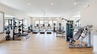 Located at 542 Gateway Centre Pkwy in North Chesterfield, VA, this fitness center offers a thoughtfully designed, single-floor workout space that accommodates a wide range of exercise needs. The interior features light hardwood-style flooring, crisp white walls, and recessed lighting complemented by ceiling fans that contribute to a clean, airy atmosphere throughout.

Large windows line the walls, flooding the space with natural light and providing views of the surrounding area, creating an open and inviting environment for exercise. The cardio zone is anchored by multiple treadmills, elliptical machines, and a stationary bike, all positioned to take advantage of the natural light from the window bank.

The strength training area is well-appointed with a cable machine, multi-functional rack, and a full dumbbell rack offering a range of weights. Functional fitness enthusiasts will find battle ropes, TRX suspension trainers, kettlebells, medicine balls, and plyo boxes ready for dynamic workouts. Stability balls and an adjustable bench round out the free weight section.

A dedicated wall-mounted display of fitness rules and a fire safety station reflect a commitment to safety and organization. The space is efficiently arranged to maximize floor area while maintaining clear workout zones, making it a comprehensive and accessible fitness facility.