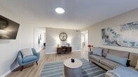 Located at 118 Broadhurst Rd in Jacksonville, NC, this single-story 2-bedroom, 1-bathroom home offers a thoughtfully designed layout with modern updates throughout. Light wood-tone flooring runs continuously across the space, contributing to a clean, cohesive aesthetic.

The living room is a welcoming, well-lit area featuring a wall-mounted TV, a skylight-style ceiling fixture, and neutral gray walls accented by a wainscoting detail. A hallway connects seamlessly to the rest of the home. The combined dining room and kitchen is efficiently arranged, featuring white shaker-style cabinetry, light stone countertops, black appliances including a gas range and full-size refrigerator, and a dedicated dining area brightened by windows with blinds and direct access to the exterior.

The primary bedroom is a comfortable retreat with panel-accented walls, ample natural light from large windows, and access to a dedicated closet. The second bedroom, also featuring a window wall and a shiplap accent wall, provides a bright and versatile space. Three closets in total offer generous storage throughout the home.

The bathroom is finished with a white vanity, solid countertop, and a wall mirror, maintaining the home's clean, neutral palette. A utility room and hallway round out the functional floor plan, making this home practical and well-organized for everyday living.