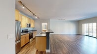Located at 144 N Jefferson St in the heart of Milwaukee, WI, this well-appointed three-bedroom, two-bathroom residence spans two floors, offering a thoughtful layout with generous living space. The main level features an open-concept living room and kitchen, anchored by expansive floor-to-ceiling windows and sliding glass doors that flood the area with natural light and provide views of the surrounding cityscape. Rich hardwood-style flooring flows throughout the main level, complementing the clean, neutral palette of the walls. The kitchen is outfitted with light maple cabinetry, stainless steel appliances including a range, microwave, and refrigerator, dark countertops, and a peninsula with a built-in sink — ideal for both cooking and casual dining. Track lighting illuminates the space efficiently. Upstairs, the bedrooms are carpeted for comfort, each featuring ceiling fans and large windows with urban views. The spacious primary bedroom is complemented by a walk-in closet with wire shelving organization. Two full bathrooms serve the residence — one with a tub-shower combination and wood-tone vanity, the other with a bright vanity mirror and wood-style flooring. A dedicated closet and staircase complete this functional, urban home.
