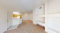This single-level space is designed with a bright, neutral palette and an open, functional layout. The living area serves as the central hub of the unit, highlighted by a corner fireplace with a tiled hearth and brass-trimmed glass doors, flanked by built-in shelving and a built-in desk that provide ample storage and workspace. Large sliding glass doors open to a private balcony with decorative iron railings, offering views of surrounding greenery and filling the living space with natural light. The entryway features tile flooring that transitions into wall-to-wall carpet throughout the main living and bedroom areas.

The kitchen is efficiently arranged in an L-shaped configuration, equipped with warm honey-toned wood cabinetry, white appliances including a gas range and built-in microwave, and light countertops. A peninsula with a raised breakfast bar connects the kitchen to the living area, creating a practical open-concept flow. Wood-look flooring runs through the kitchen, adding visual contrast.

The bedrooms are generously proportioned, each carpeted and filled with natural light from windows fitted with vertical blinds. The rooms feature clean white walls and ceiling-mounted HVAC vents, contributing to a consistently comfortable and well-ventilated environment throughout the space.