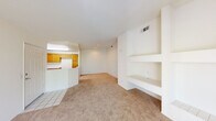 This single-level space is designed with a bright, neutral palette and an open, functional layout. The living area serves as the central hub of the unit, highlighted by a corner fireplace with a tiled hearth and brass-trimmed glass doors, flanked by built-in shelving and a built-in desk that provide ample storage and workspace. Large sliding glass doors open to a private balcony with decorative iron railings, offering views of surrounding greenery and filling the living space with natural light. The entryway features tile flooring that transitions into wall-to-wall carpet throughout the main living and bedroom areas.

The kitchen is efficiently arranged in an L-shaped configuration, equipped with warm honey-toned wood cabinetry, white appliances including a gas range and built-in microwave, and light countertops. A peninsula with a raised breakfast bar connects the kitchen to the living area, creating a practical open-concept flow. Wood-look flooring runs through the kitchen, adding visual contrast.

The bedrooms are generously proportioned, each carpeted and filled with natural light from windows fitted with vertical blinds. The rooms feature clean white walls and ceiling-mounted HVAC vents, contributing to a consistently comfortable and well-ventilated environment throughout the space.