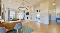 Located along Interstate 10 in Boerne, Texas, this expansive single-story community facility offers a thoughtfully designed layout encompassing a diverse range of amenity spaces. The centerpiece is a grand lounge featuring soaring ceilings, elegant herringbone-patterned hardwood flooring, and a dramatic floor-to-ceiling limestone fireplace flanked by built-in shelving. Two large wrought-iron candle-style chandeliers anchor the space, while an abundance of natural light pours in through black-framed windows that overlook the covered exterior corridor. The exterior façade showcases natural limestone masonry and bold green structural columns beneath a wood-paneled ceiling, creating an inviting transitional space that connects indoors and outdoors. A bright dining area accommodates multiple seating arrangements and opens to outdoor views through large windows and glass doors. The fitness center is well-equipped with cardio machines, ceiling fans, and ample natural light. A dedicated co-working office features a long built-in desk with a vibrant green accent wall and herringbone flooring. A children's playroom offers a welcoming, colorful environment with storage and a wall-mounted display. Two bathrooms and a utility room round out the functional offerings, while an outdoor swimming pool with a fenced surround and adjacent covered lounge area completes this full-service community hub.