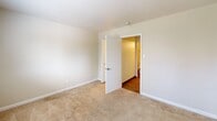 This compact two-bedroom unit in Affton, Missouri offers a practical, efficiently designed single-floor layout. The kitchen features wood-look plank flooring, dark wood cabinetry, a black refrigerator, a sink with under-counter storage, and overhead cabinets — providing functional workspace within a modest footprint. A ceiling-mounted light fixture keeps the area well-lit.

Both bedrooms are carpeted and finished with neutral beige walls and white trim baseboards. The primary bedroom is the larger of the two, offering enough space for standard bedroom furnishings. Each room includes a window with blinds, allowing natural light and outdoor views of the surrounding greenery. Baseboard heaters run along the walls, and the primary bedroom also features a wall-mounted air conditioning unit for year-round climate control.

The bathroom is clean and straightforward, featuring a full-size white soaking tub with a combination shower, a tiled surround with a built-in niche, and a curtain rod overhead. The overall layout, as seen in the floor plan overview, connects the rooms in a logical flow, with wood-look flooring in the common areas transitioning to carpet in the bedrooms. The unit offers a no-frills, functional living space suitable for individuals or small households.