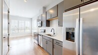 This thoughtfully designed unit at 710 Grandview Crossing Way in Columbus, Ohio, offers a compact yet functional layout ideal for urban living. The open-plan kitchen and living area form the heart of the space, finished with warm-toned hardwood-style flooring that runs throughout and light gray walls that create a clean, modern aesthetic. The kitchen is well-appointed with sleek gray cabinetry featuring matte black hardware, white quartz countertops, a white subway tile backsplash, and a full suite of stainless steel appliances, including a refrigerator with an in-door ice and water dispenser, electric range, over-the-range microwave, and dishwasher. A single-basin sink with a matte black faucet adds a stylish, coordinated touch. The living area benefits from natural light streaming through a large window fitted with white blinds, offering views of the surrounding Columbus neighborhood. The full bathroom is clean and functional, featuring light tile flooring, a tub/shower combination with a curved rod, and matte black fixtures that echo the design language of the kitchen. The unit's efficient layout and modern finishes make it a practical and attractive space in the heart of Columbus.