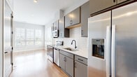 This thoughtfully designed unit at 710 Grandview Crossing Way in Columbus, Ohio, offers a compact yet functional layout ideal for urban living. The open-plan kitchen and living area form the heart of the space, finished with warm-toned hardwood-style flooring that runs throughout and light gray walls that create a clean, modern aesthetic. The kitchen is well-appointed with sleek gray cabinetry featuring matte black hardware, white quartz countertops, a white subway tile backsplash, and a full suite of stainless steel appliances, including a refrigerator with an in-door ice and water dispenser, electric range, over-the-range microwave, and dishwasher. A single-basin sink with a matte black faucet adds a stylish, coordinated touch. The living area benefits from natural light streaming through a large window fitted with white blinds, offering views of the surrounding Columbus neighborhood. The full bathroom is clean and functional, featuring light tile flooring, a tub/shower combination with a curved rod, and matte black fixtures that echo the design language of the kitchen. The unit's efficient layout and modern finishes make it a practical and attractive space in the heart of Columbus.