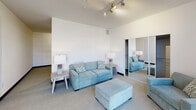 Located at 888 N Main St in Santa Ana, California, this single-floor residence offers a thoughtfully designed layout with a contemporary aesthetic throughout. The living area features plush carpeting, crisp white walls, and impressive floor-to-ceiling windows dressed with vertical blinds, allowing an abundance of natural light and providing open views of the surrounding streetscape. A second lounge area showcases exposed ductwork along the ceiling, lending an industrial character to the space. The bedroom is generously proportioned with soaring ceilings, track lighting, and mirrored sliding closet doors that enhance the sense of space and brightness. The kitchen is well-equipped with dark espresso cabinetry, marble-look countertops, light wood-style flooring, and stainless steel appliances including a range, over-the-range microwave, and dishwasher. The bathroom features rich wood-toned cabinetry, a single-sink vanity with a large mirror, wall sconce lighting, and a glass-enclosed walk-in shower. Together, these spaces create a cohesive, modern living environment that balances functionality with clean, contemporary design details throughout.