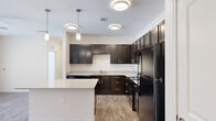 This single-floor residence is designed with a clean, contemporary aesthetic and a practical open-concept layout. The kitchen serves as a central highlight, outfitted with rich dark espresso cabinetry, granite-style countertops, and a full suite of black appliances, including a refrigerator, range, microwave, and dishwasher. A large center island with pendant lighting above provides additional prep space and casual seating, while wood-look flooring ties the kitchen seamlessly into the adjacent living area. The living space is bright and open, featuring a ceiling fan, wood-look flooring, and French doors that invite natural light and provide outdoor access.

The bedrooms are comfortably sized, finished with the same light wood-look flooring and ceiling fans. One bedroom features a walk-in closet with built-in shelving, while another includes a double-door closet. The bathrooms reflect consistent attention to detail — one features a glass-enclosed walk-in shower with white subway tile and brushed nickel fixtures, while another includes a granite-topped vanity with dark cabinetry and an adjacent walk-in closet with open shelving. Neutral tones throughout create a cohesive, welcoming ambiance.